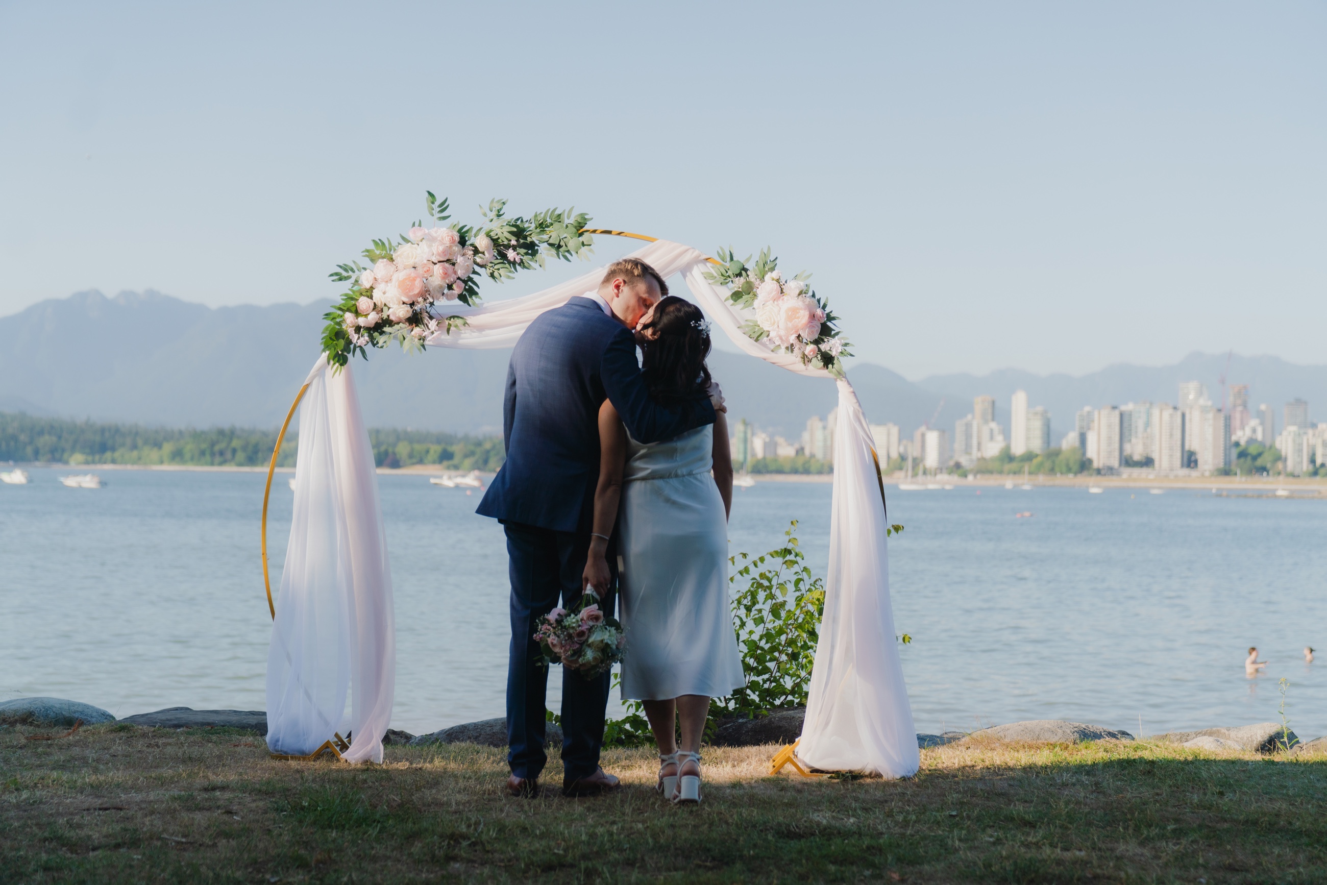 Newlyweds kissing beneath a floral arch on the Vancouver waterfront