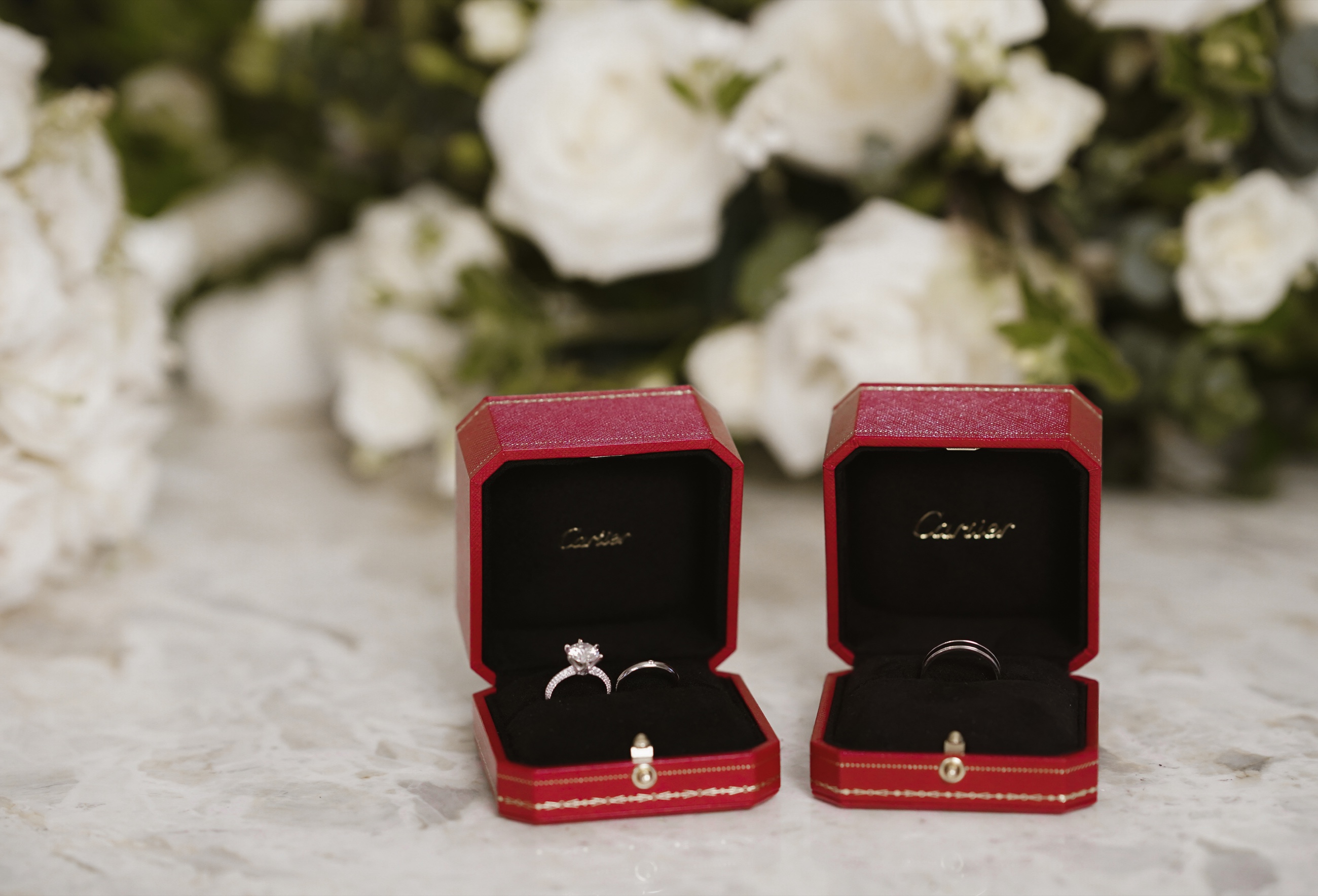 Wedding rings displayed in red boxes before white flowers